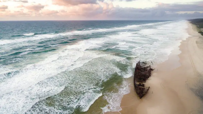 Iconic rusted shipwreck on Fraser Island’s sandy shore at sunset, highlighted during the Fraser Experience Tour beneath dramatic clouds.