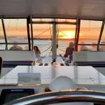 Stunning sunset view from catamaran cockpit on Sydney Harbour BYO Sunset Sparkle Cruise, guests relaxing and enjoying skyline.