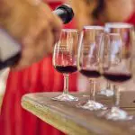 Enjoying a Full Day Swan Valley Wine Tour as someone pours rich red wine, with guests in striking red dresses mingling in the background.