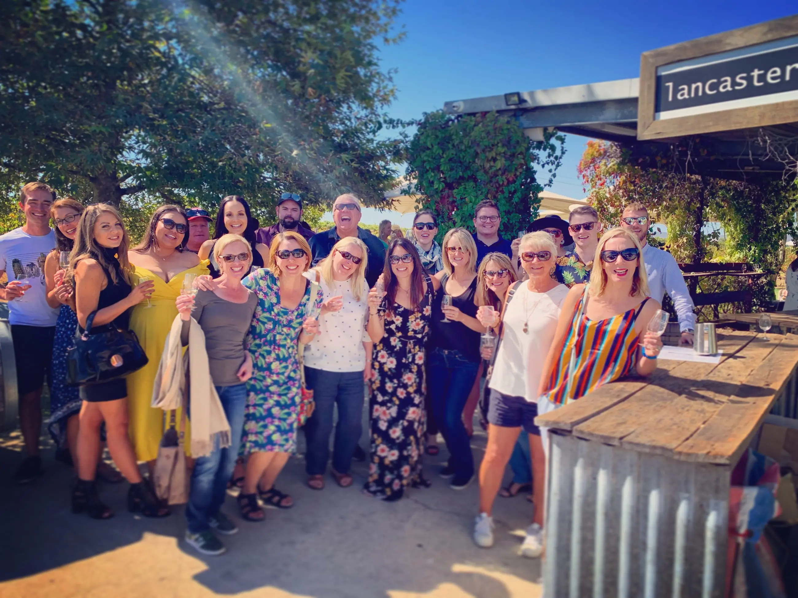 Happy group enjoying wine and sunshine at rustic bar during Half Day Swan Valley Wine Tour, surrounded by scenic outdoor views.