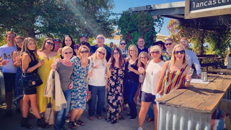 Happy group enjoying wine and sunshine at rustic bar during Half Day Swan Valley Wine Tour, surrounded by scenic outdoor views.