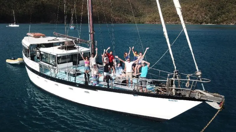 Friends enjoying the Habibi 2 Day 1 Night Whitsunday Sailing adventure, anchored in turquoise waters beside lush green hills.