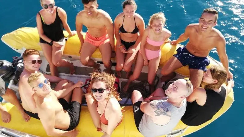 Smiling young adults in swimwear relax on a vibrant yellow Big Fury Whitsundays boat cruising through crystal-clear blue ocean waters.
