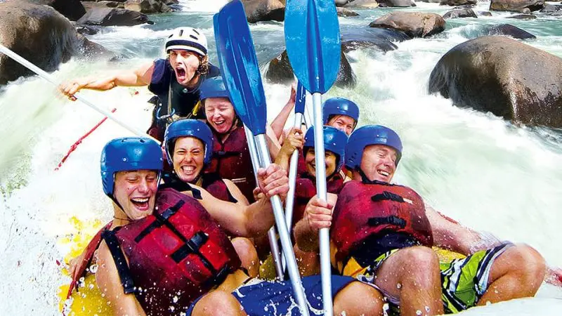 Group of six adventurers paddling and laughing through intense Tully River rapids on a 1 Day White Water Rafting Raging Thunder tour.