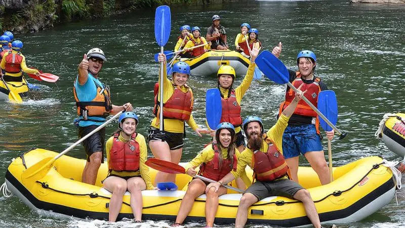 Thrill-seekers white water raft Barron River with Raging Thunder, smiling by stunning waterfall on a half-day adventure tour.