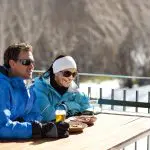 Two travellers in winter jackets savour snacks and drinks after a Lake Mountain Snow Waterfalls Tour near Melbourne, enjoying the scenery.