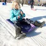 Happy child in a vibrant blue coat rides a purple sledge on snowy Lake Mountain during a 1 Day Snow Tour from Melbourne.