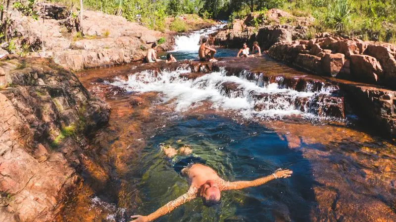 Visitors enjoy swimming and relaxing in a crystal-clear rocky stream under the sun on a Litchfield National Park Crocodile Cruise tour.