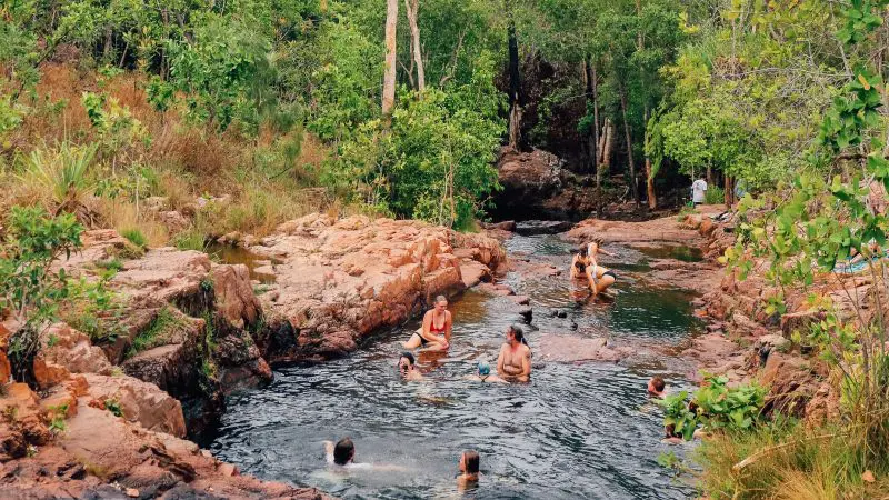 Visitors swim and unwind in a scenic natural rock pool during a 1 Day Litchfield National Park and Fogg Dam Wetlands tour adventure.