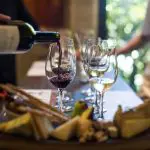 A person pours rich red wine next to elegant white wine glasses and gourmet cheese on a premium 1 Day Hunter Valley Wine Tour.