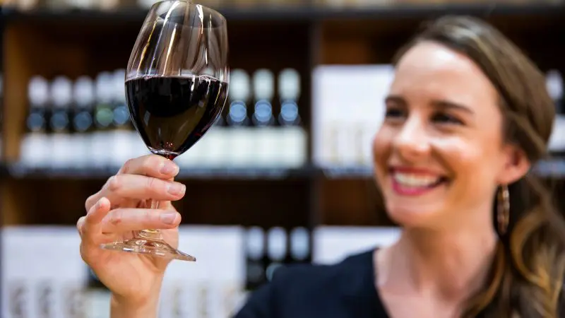 A joyful woman savours a glass of red wine, surrounded by bottles, during a scenic 1-day Hunter Valley Wine Tour experience.