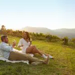 A couple enjoys a scenic sunset picnic on a blanket in Hunter Valley’s vineyard during an exclusive 1 Day Wine Tour experience.