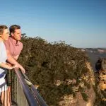 Happy couple admires stunning Blue Mountains sunset views on a 1 Day Wilderness Tour, clear sky above, perfect for adventure seekers.