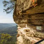 Two travellers at a Blue Mountains lookout enjoy panoramic sunset views of lush forested valleys on a 1 Day Wilderness Tour.
