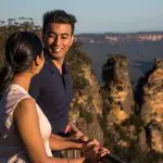 Smiling couple taking in panoramic views of rocky cliffs and lush peaks on a Blue Mountains Sunset Wilderness Tour, 1-day adventure.