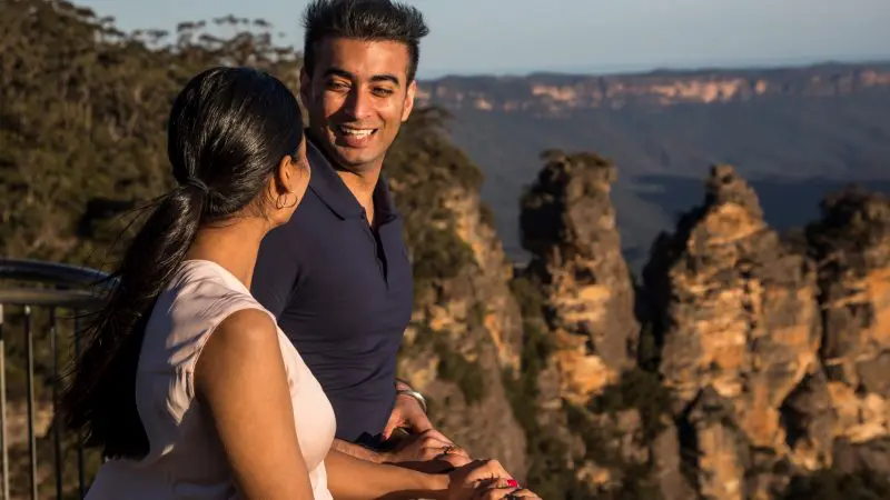 Smiling couple taking in panoramic views of rocky cliffs and lush peaks on a Blue Mountains Sunset Wilderness Tour, 1-day adventure.