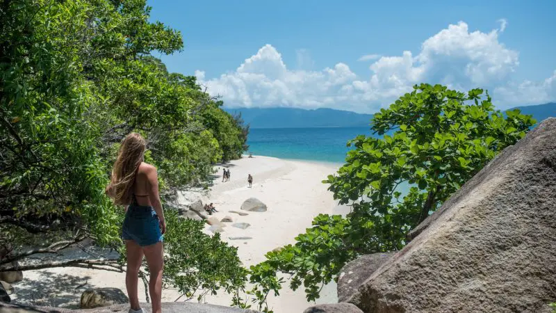 Woman standing on rocky shore, gazing at Fitzroy Island’s pristine beach and turquoise sea during a top-rated half-day tour.