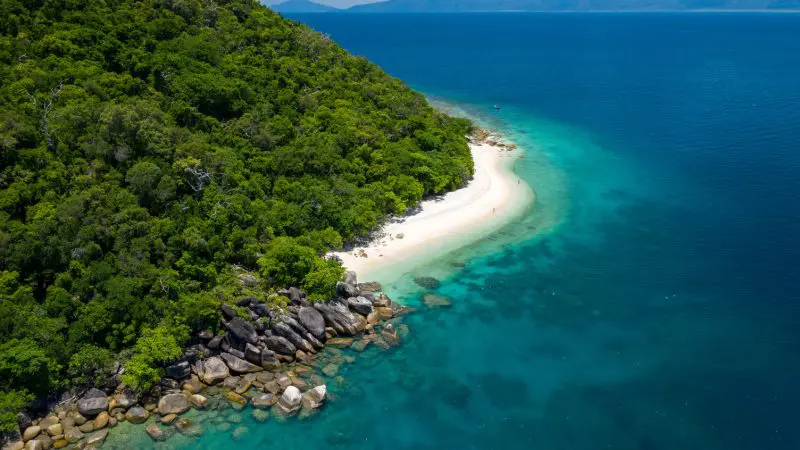Stunning aerial view of Fitzroy Island Half Day Tour—pristine sandy beach, vibrant lush coastline, and crystal-clear blue-green sea.