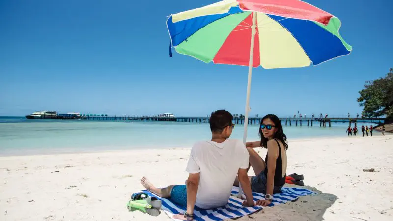 A couple relaxes beneath a vibrant umbrella on a sunny day, waiting for their Half-Day Green Island tour with 1pm departure.