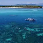 Ocean Free sailboat by Green Island coral reef, vibrant snorkellers enjoying clear blue waters on a Great Barrier Reef day tour adventure.