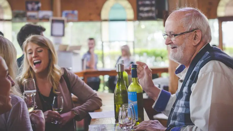 Friends share laughter and wine at a sunlit, intimate restaurant during a Hunter Valley 1 Day Wine Tour experience.