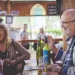 An older man and young woman share laughter during a Hunter Valley Wine Tour in a cosy, sunlit restaurant, enjoying their experience.