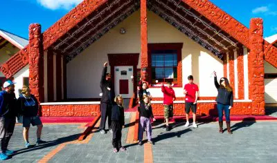 Smiling group outside an iconic Māori meeting house following a renowned Whakarewarewa Cultural Performance in Rotorua, New Zealand.