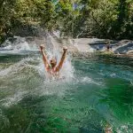 Adventurer plunging joyfully into a vibrant green river—discover this thrill on a top-rated 1 Day Waterfall and Rainforest Tour.