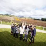 Smiling group poses in front of lush Yarra Valley vineyards during wine tour, capturing unforgettable winery experience moments together.
