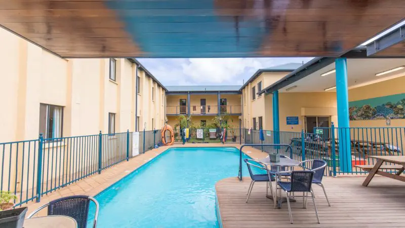 Modern outdoor hotel pool area features inviting tables, chairs, and blue fencing—ideal for Perth to Exmouth tour hostel twin stays.