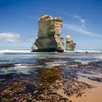 Majestic limestone sea stacks tower near a pristine sandy beach, iconic sights on the 1 Day Great Ocean Road Rainforest Tour.