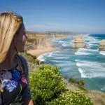 Blonde woman admires breathtaking ocean views on a sunny Great Ocean Road Reverse Eco Tour near iconic Twelve Apostles, Australia.