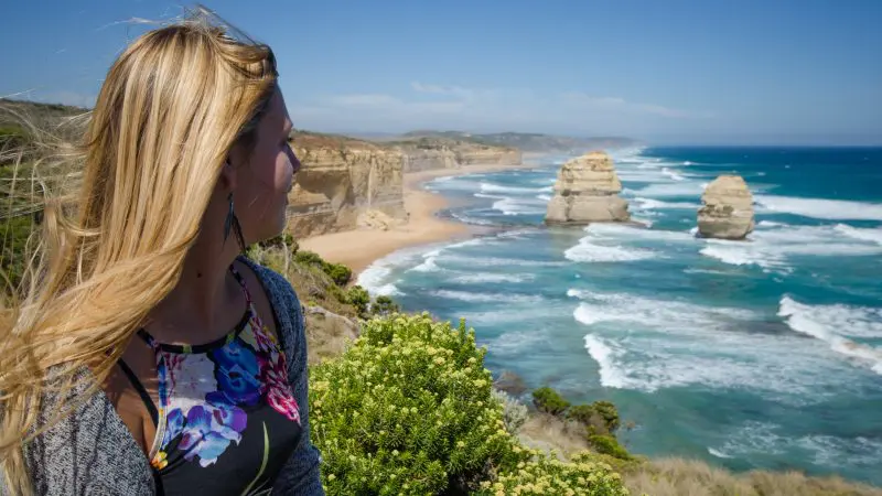 Blonde woman gazes over the iconic Great Ocean Road during a 2-day Melbourne to Adelaide overland tour, featuring stunning coastal views.