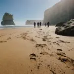 Group of five enjoying a scenic walk on a sandy beach with dramatic cliffs at sunset during a 1 Day Great Ocean Road Tour from Melbourne.