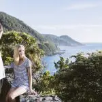 Couple admires lush green hills and sweeping sea views on a sunny Great Ocean Road Reverse Eco Tour, perfect for nature lovers.