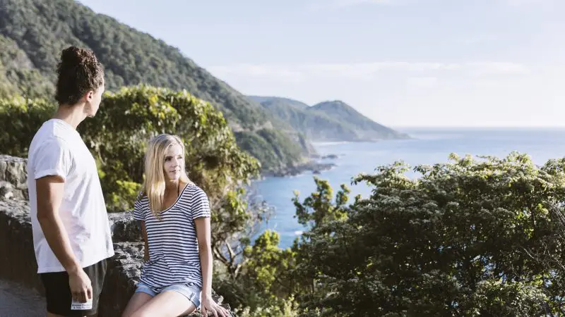 Two travellers admire stunning coastal scenery, lush rainforest, and vibrant blue ocean on a 1 Day Great Ocean Road Rainforest Tour.