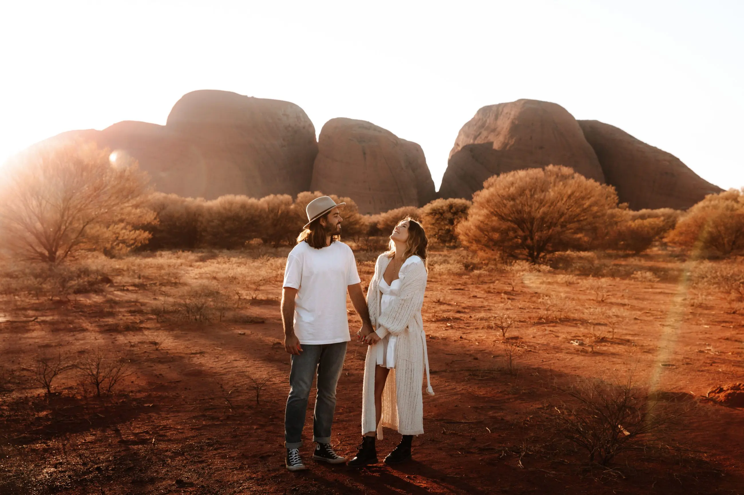 A couple holding hands among iconic Uluru Kata Tjuta desert rocks, bathed in sunlight on a 2-day tour from Ayers Rock Yulara.