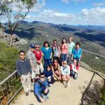Travellers on the 3 Day Great Ocean Road Melbourne to Adelaide tour pose atop a scenic overlook with panoramic blue sky views.