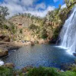 Scenic waterfall cascades into a rocky pool on the 3 Day Great Ocean Road Grampians Explorer, framed by a dramatic, partly cloudy sky.
