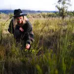 Woman in a sunhat forages wild plants in lush grass during her 2 Day Great Ocean Road journey from Melbourne to Adelaide adventure.