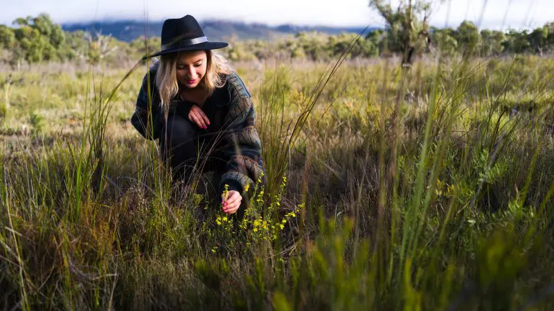 Woman in black hat explores lush field plants under clear skies on a vibrant 2 Day Great Ocean Road Grampians adventure tour.