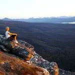 A woman relaxes on a rugged cliff, admiring the sunset during a 3-day Great Ocean Road tour from Adelaide to Melbourne, Australia.