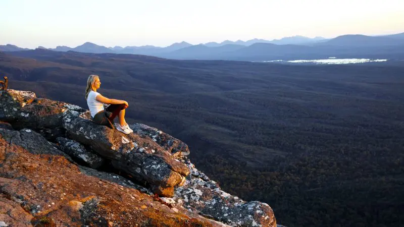 A woman relaxes on a rugged cliff, admiring the sunset during a 3-day Great Ocean Road tour from Adelaide to Melbourne, Australia.