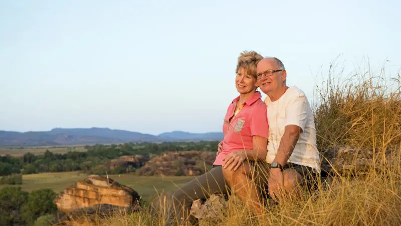 Senior couple relaxing on a lush hill during a 1 Day Kakadu Wilderness Escape with Fogg Dam Wetlands, surrounded by scenic nature.
