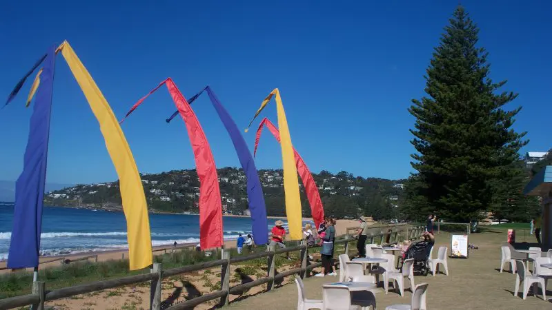 Vibrant tall flags flutter by a scenic beachside lounge on a 1 Day Home Away Tour, set below a clear blue sky for relaxation.