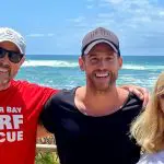 Three people smile by the sea in Summer Bay Surf Rescue shirts during a Celebtime Tours 1 Day Home and Away experience.