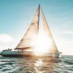 Experience the Broomstick 2 Day 2 Night Whitsunday Sailing boat gliding at sunset, golden sunlight streaming through sleek white sails.