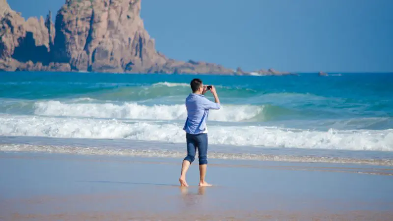 Barefoot visitor in rolled-up trousers photographs scenic waves on Phillip Island beach at sunset before the famous Penguin Parade begins.