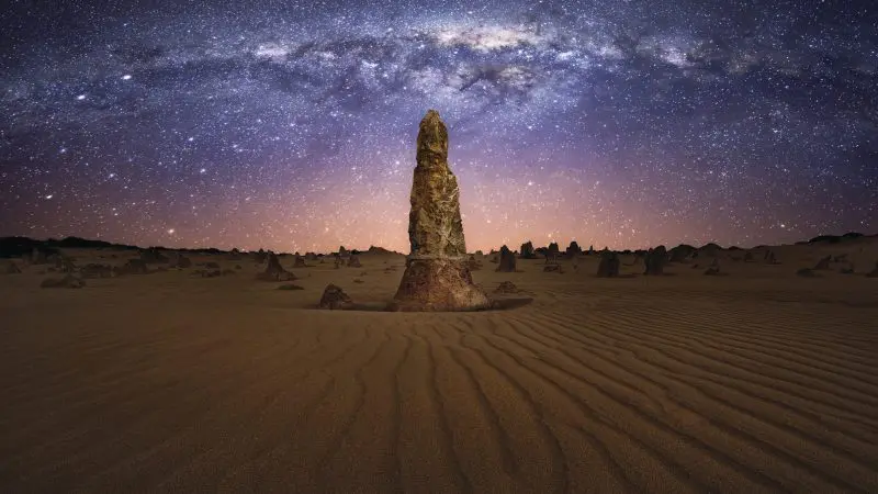 Towering rock formation on golden desert sands beneath the star-studded Milky Way, ideal for a Pinnacles Sunset Stargazing Tour.