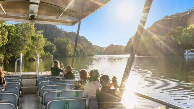 Travellers on the 4 Day Kakadu Katherine Gorge Experience boat tour photograph the sparkling sunlit river and vibrant green hills.
